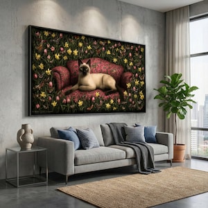 Op de afbeelding: Een ingelijst kunstwerk toont een Siamees kat die op een rode bloemenbank ligt, omringd door gele en roze bloemen. Het kunstwerk hangt boven een grijze bank met blauwe kussens en een geweven vloerkleed, wat een gezellige woonkamer creëert.