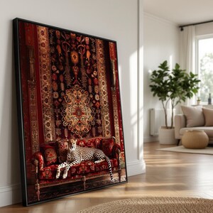 May include: A framed print depicting a cheetah lounging on a red sofa, set against a backdrop of a detailed red and gold tapestry. The artwork is propped against a white wall in a bright room.
