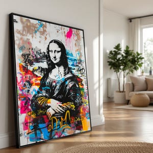 May include: A framed art print of the Mona Lisa, overlaid with graffiti art. The black and white portrait is contrasted with vibrant splashes of pink, yellow, blue, and orange paint, and graffiti-style lettering. The artwork is displayed in a black frame.