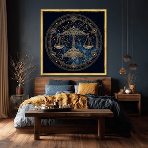 Op de afbeelding: Een ingelijst kunstwerk met het Weegschaal sterrenbeeld in goud tegen een donkerblauwe, sterrenhemel achtergrond. Het vierkante kunstwerk hangt boven een houten bed met blauwe en gouden beddengoed. De kamer heeft een donkere esthetiek.