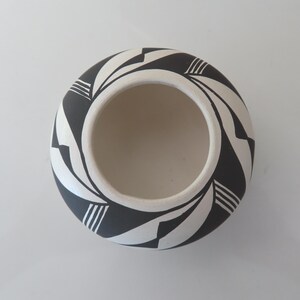 May include: A round, ceramic bowl with a cream-colored interior and a black and white geometric pattern around the exterior. The design features alternating black and white shapes, creating a spiral effect. The bowl is viewed from above.