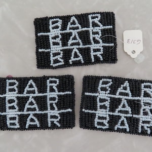 May include: Three black and white beaded rectangular coasters with the word "BAR" spelled out in a grid pattern. The coasters have white tags with black text that reads "E/E57" and "G/31".
