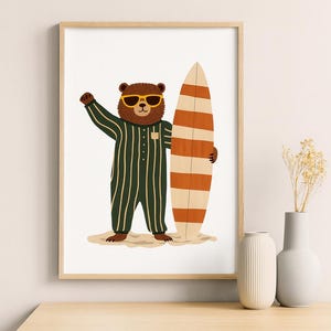 Puede incluir: Impresión enmarcada de un oso de dibujos animados con gafas de sol y un mono a rayas verdes, sosteniendo una tabla de surf con rayas naranjas y blancas. El oso está sobre una ilustración de playa arenosa.