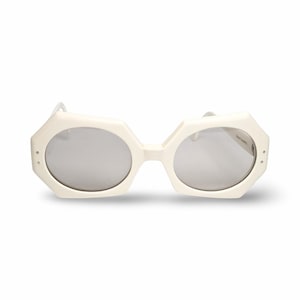 May include: White sunglasses with a unique geometric frame and oval lenses. The sunglasses have a distinctive shape, with a series of angles and curves. The lenses are a light silver color, and the frame is a solid, opaque white.