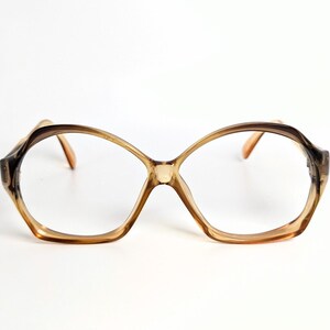 May include: Vintage oversized eyeglasses with a geometric shape. The frames are a gradient of brown and tan, with clear lenses. The arms are a light brown color. The glasses are set against a white background.