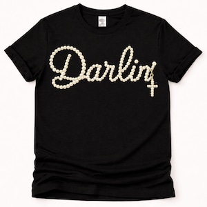 May include: A white ceramic mug with a black handle and the text "But First, Coffee" in a bold, black font. The mug is set against a blurred background, suggesting a cozy setting.