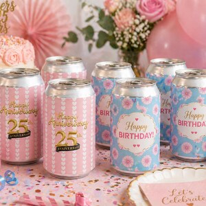 May include: Pink and blue decorated beverage cans for a birthday or anniversary celebration. Some cans say "Happy Anniversary 25" in gold lettering, while others say "Happy Birthday!" with floral designs.
