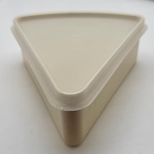 May include: A beige, triangular food storage container with a matching lid. The container has a smooth, matte finish and a simple, geometric design. The lid fits snugly, creating an airtight seal. Ideal for storing leftovers or packing snacks.