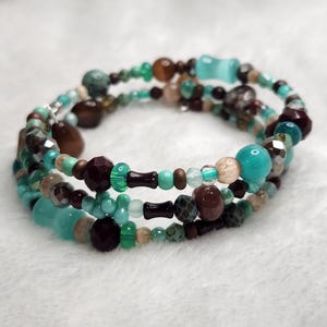 May include: A multi-strand wrap bracelet featuring a variety of beads in shades of turquoise, dark brown, and tan. The design includes faceted, smooth, and textured round beads, along with cylindrical and uniquely shaped accent pieces.