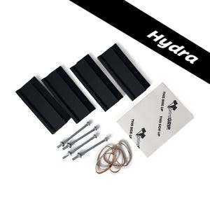 May include: Four black rectangular mounting brackets, four silver metal bolts with nuts, a small bundle of tan rubber bands, and a white square adhesive pad labeled printGRIP with the text THIS SIDE UP. A black diagonal banner displays Hydra.