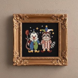 Può includere: Opera d'arte a punto croce in una cornice dorata ornata. L'opera presenta due personaggi stravaganti: un clown con un palloncino e un procione in un abito a righe. Lo sfondo è nero e i personaggi si tengono per mano. L'opera è firmata "VelourPeachXStitch".