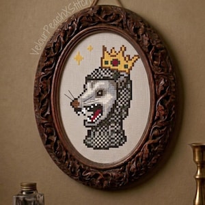 Könnte beinhalten: Oval gerahmtes Kreuzstich-Kunstwerk mit einem Opossum, das eine goldene Krone trägt. Das Opossum hat ein detailliertes, pixeliges Design mit einem grimmigen Gesichtsausdruck. Der Rahmen ist dunkelbraun mit kunstvollen Schnitzereien.