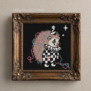Könnte beinhalten: Eine Kreuzstichstickerei, die einen Igel als Clown verkleidet mit schwarz-weiß kariertem Outfit und Halskrause auf schwarzem Hintergrund zeigt, gerahmt in einem verzierten, dunkelbraunen Holzrahmen im Vintage-Stil.