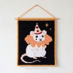 Puede incluir: Un tapiz de ganchillo rectangular que muestra un ratón blanco con un cuello de volantes color melocotón y un gorro de fiesta crema con puntos rojos. El ratón está sobre un fondo negro con estrellas amarillas y el texto VelourPeachXStitch.