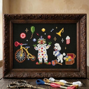 May include: Cross-stitch artwork in a dark brown ornate frame. The artwork features a clown, a bicycle, a poodle, and circus-themed elements like balloons and popcorn. The color palette includes red, yellow, green, and white on a black background.
