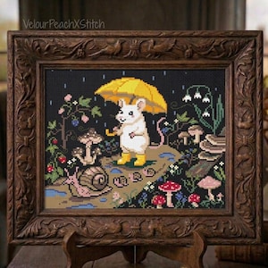 Puede incluir: Un bordado de punto de cruz en un marco de madera ornamentado de color marrón oscuro que muestra un ratón blanco con un paraguas amarillo y botas amarillas, bajo la lluvia con setas, un caracol y flores. El texto VelourPeachXStitch está arriba.