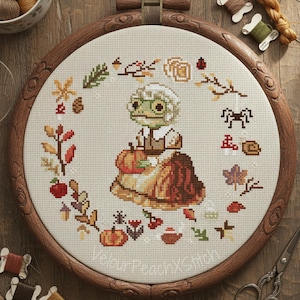 Könnte beinhalten: Kreuzstich-Stickerei mit einem skurrilen Frosch-Charakter in einem Herbst-Design. Der Frosch trägt ein Kleid und hält einen Kürbis, umgeben von Herbstblättern und saisonalen Elementen. Die Stickerei befindet sich in einem Holzreifen.