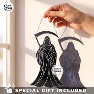 May include: A black stained glass suncatcher depicting a hooded grim reaper figure holding a scythe, suspended by a silver metal chain. The glass features a textured surface with silver solder lines and a small white sticker reading HOPPY LICENCE.