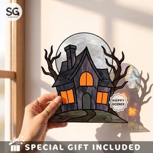 May include: A stained glass suncatcher featuring a dark purple haunted house silhouette against a large white moon, flanked by bare black trees. The house has glowing orange windows and a small white label with the text HOPPY LICENCE.