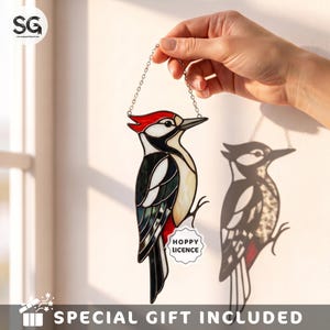 May include: A stained glass woodpecker suncatcher featuring black, white, and red glass segments with a silver metal chain for hanging. A small white scalloped tag attached to the bird displays the black text HOPPY LICENCE in a bold font.