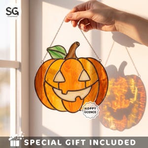 May include: A stained glass pumpkin suncatcher featuring orange glass panels, a green leaf, and a brown stem. The pumpkin has a carved jack-o'-lantern face with triangular eyes and a jagged mouth. A small white tag reads HOPPY LICENCE.