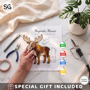 May include: A stained glass moose suncatcher featuring brown and cream glass pieces with dark solder lines. The design is displayed over a paper pattern labelled Majestic Moose Premium Handcrafted Stained Glass Design with JPG, PDF, PNG, and SVG icons.