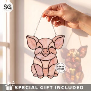 May include: A stained glass suncatcher shaped like a pig with light pink marbled glass panels and dark metal solder lines. The pig has large ears and a smiling expression. A silver chain is attached to the top for hanging. Text reads HOPPY LICENCE.