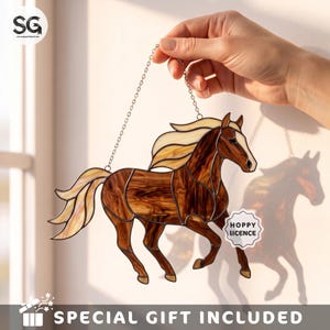 May include: A stained glass suncatcher shaped like a horse with a brown body and cream-colored mane and tail. The piece features dark metal soldering lines and hangs from a silver-toned chain. A small white tag reads HOPPY LICENCE.
