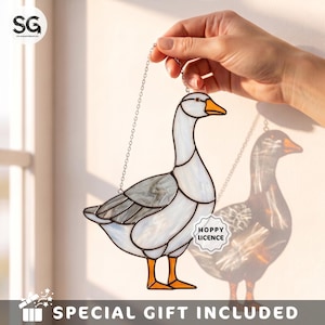 May include: A stained glass goose suncatcher featuring white and grey marbled glass panels with orange glass feet and beak. The piece is suspended by a silver metal chain and includes a small white tag with the text HOPPY LICENCE attached.
