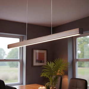 Puede incluir: Una lámpara colgante rectangular de madera con una fuente de luz LED lineal y brillante. La lámpara está suspendida del techo por dos finos cables. La luz es de color blanco cálido y la madera tiene una veta natural. La lámpara mide aproximadamente 122 cm de largo.
