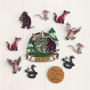 May include: A collection of whimsical character cutouts, including a brown Gruffalo, a mouse, a fox, an owl, and a snake. A centerpiece features a forest scene with the number 4 and the name "Oliver". A brown, scalloped-edge tag reads "There's no such thing as a Gruffalo..."