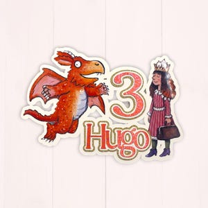 Peut inclure: Décoration de gâteau d'anniversaire fantaisiste avec un dragon rouge, une fille couronnée et le chiffre "3" avec le nom "Hugo". Le dragon a des écailles et des ailes orange et rouges. La fille porte une robe rayée rouge et blanche.