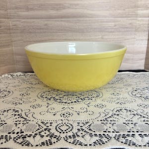 May include: A round mixing bowl with a smooth, glossy yellow exterior and a white interior. The bowl features a wide, open top and a tapered base, constructed from a solid, opaque material with a clean, simple design and no additional patterns.
