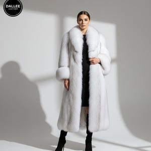 Puede incluir: Un abrigo largo de piel blanca con un cuello ancho y puños a juego. El abrigo se lleva sobre un vestido negro y se combina con botas negras de tacón alto. El logotipo de Dallee Leather es visible.
