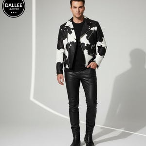 Könnte beinhalten: Eine schwarz-weiß bedruckte Lederjacke im Kuhfell-Design mit Reißverschluss. Die Jacke wird mit einer schwarzen Lederhose und schwarzen Stiefeln kombiniert. Das Bild enthält den Text "DALLEE LEATHER" in einem kreisförmigen Logo.