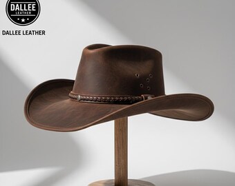 Può includere: Cappello da cowboy in pelle marrone con fascia intrecciata e occhielli. Il cappello è esposto su un supporto di legno. Il logo "DALLEE LEATHER" è visibile in alto a sinistra.