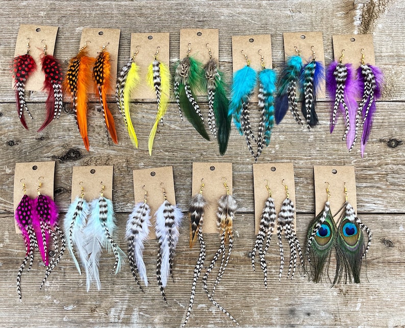 May include: Assortment of feather earrings displayed on cards. The earrings feature various colors and patterns, including black and white, red, orange, yellow, green, blue, purple, and peacock feathers.