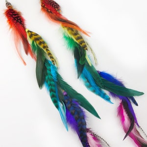 May include: A pair of long, colorful feather earrings. The earrings are made with a variety of feathers in shades of red, orange, yellow, green, blue, purple, and pink. The feathers are arranged in a cascading pattern, with the longest feathers at the bottom. The earrings are attached to silver hooks.