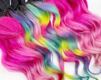 May include: A set of wavy hair extensions with a black base and a gradient of pink, teal, yellow, and purple.
