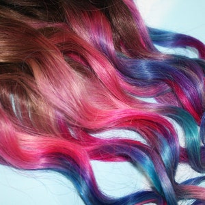 K&ouml;nnte beinhalten: Eine lange, gewellte Haarverl&auml;ngerung mit braunem Ansatz und Ombre-Farbverlauf von Pink &uuml;ber Lila zu Blau.