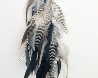 May include: A long, black and white feather hair clip with a silver clip. The feathers are arranged in a cascading style, with the black feathers at the bottom and the white feathers at the top.