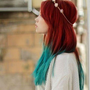 May include: A woman with long, straight hair that is red on top and teal on the bottom. She is wearing a white sweater and a flower crown.