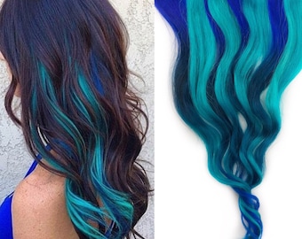 May include: Blue and teal clip-in hair extensions. The extensions are wavy and have a gradient color effect, transitioning from dark blue to teal.