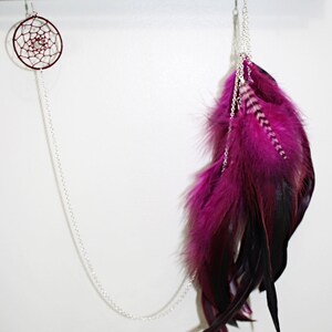 May include: A pair of earrings with a silver chain and a pink and black feather design. The earrings are hanging from a wooden rod.