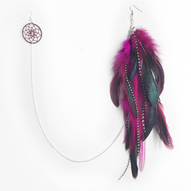May include: A pair of long, dangling earrings with a silver chain and pink and green feathers. The earrings feature a small dreamcatcher charm at the top.