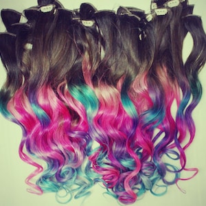 K&ouml;nnte beinhalten: Ein Set welliger Haarverl&auml;ngerungen mit einer dunkelbraunen Basis und einem Ombre-Farbverlauf von Pink &uuml;ber T&uuml;rkis zu Lila.