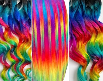 May include: Rainbow ombre hair extensions with a straight and wavy style. The hair is dyed in a vibrant rainbow pattern with shades of blue, green, yellow, orange, red, and purple.