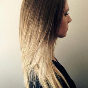 May include: A woman with long, straight hair that is ombre, transitioning from brown to blonde. The hair is styled with layers and is parted on the side.