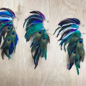 Puede incluir: Tres pu&ntilde;os decorativos para las orejas con dise&ntilde;o de plumas. Cada pu&ntilde;o presenta una combinaci&oacute;n de plumas azules, turquesas y moradas, incluyendo plumas de pavo real. Los pu&ntilde;os est&aacute;n sujetos a un clip de metal plateado.