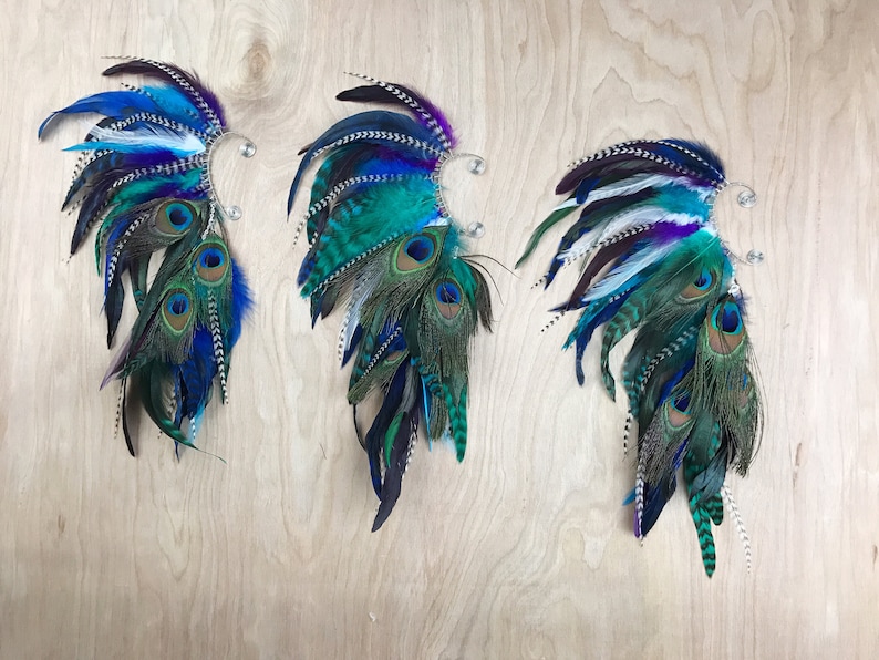 Puede incluir: Tres pu&ntilde;os decorativos para las orejas con dise&ntilde;o de plumas. Cada pu&ntilde;o presenta una combinaci&oacute;n de plumas azules, turquesas y moradas, incluyendo plumas de pavo real. Los pu&ntilde;os est&aacute;n sujetos a un clip de metal plateado.